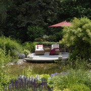 rundes Holzdeck mit Sonnenliegen und Teich mit glasklarem Wasser