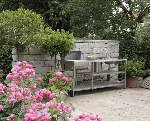 Outdoor-Küche aus Edelstahl vor gartenmauer aus Naturstein